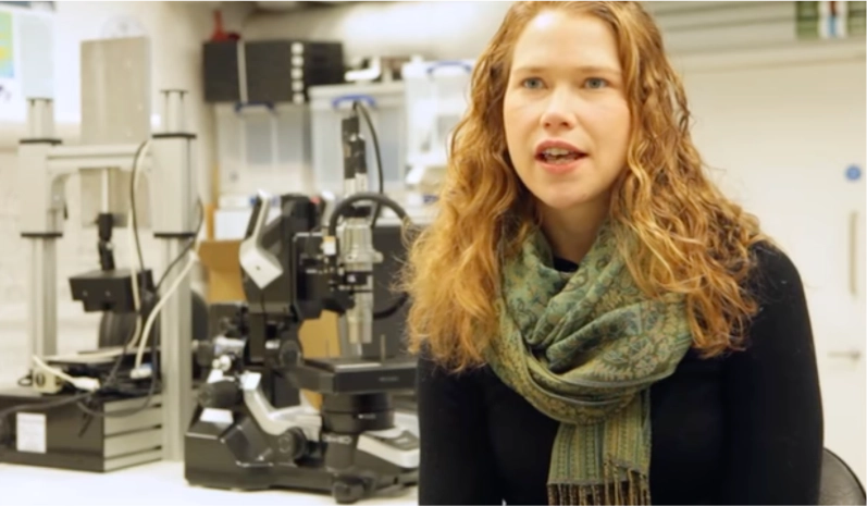Woman speaks to the camera in front of a lab